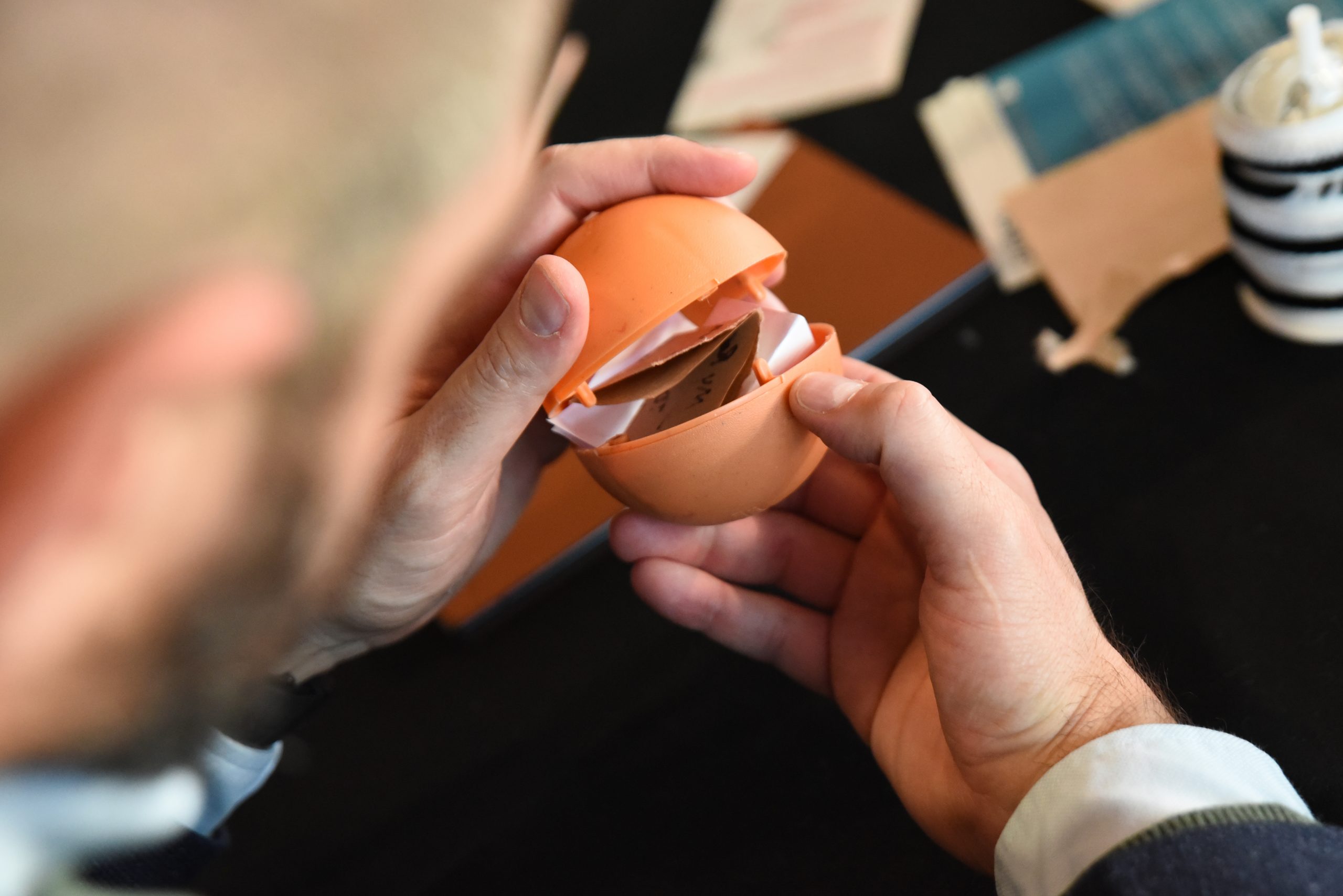 Close-up of person's hands holding open a plastic sphere containing folded pieces of paper